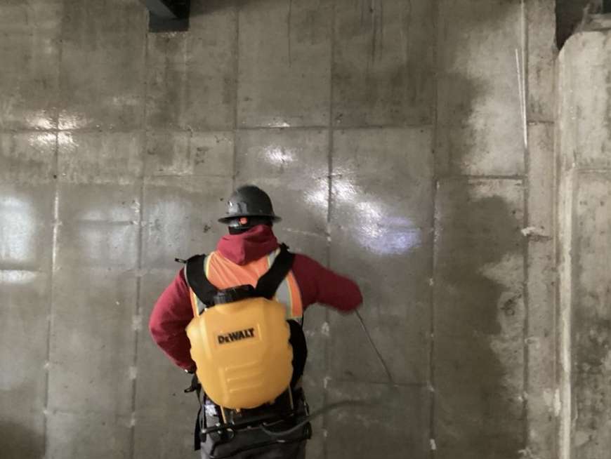 Construction worker applying Alchemco product to a concrete wall, demonstrating the product's use in surface treatment.
