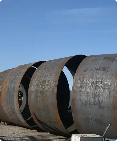 Large rusted steel pipe sections lying outdoors under a clear blue sky.